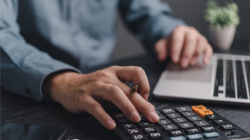 Business owner calculating equipment downtime costs on a calculator and laptop