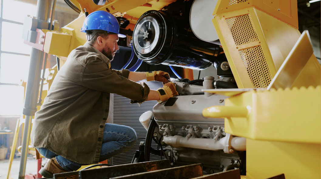 Mechanic in a hard hat servicing a yellow machine's engine