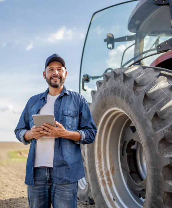 Farmer holding a tablet next to a tractor